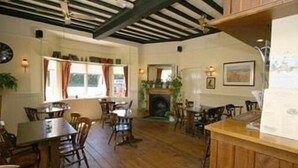 A cozy dining area with wooden tables and chairs, a fireplace, and a view of the outdoors through large windows. - The Bolingbroke Hotel (Swindon)