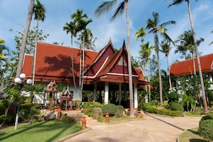 Un edificio tradizionale thailandese con tetto rosso, circondato da palme e un giardino curato.