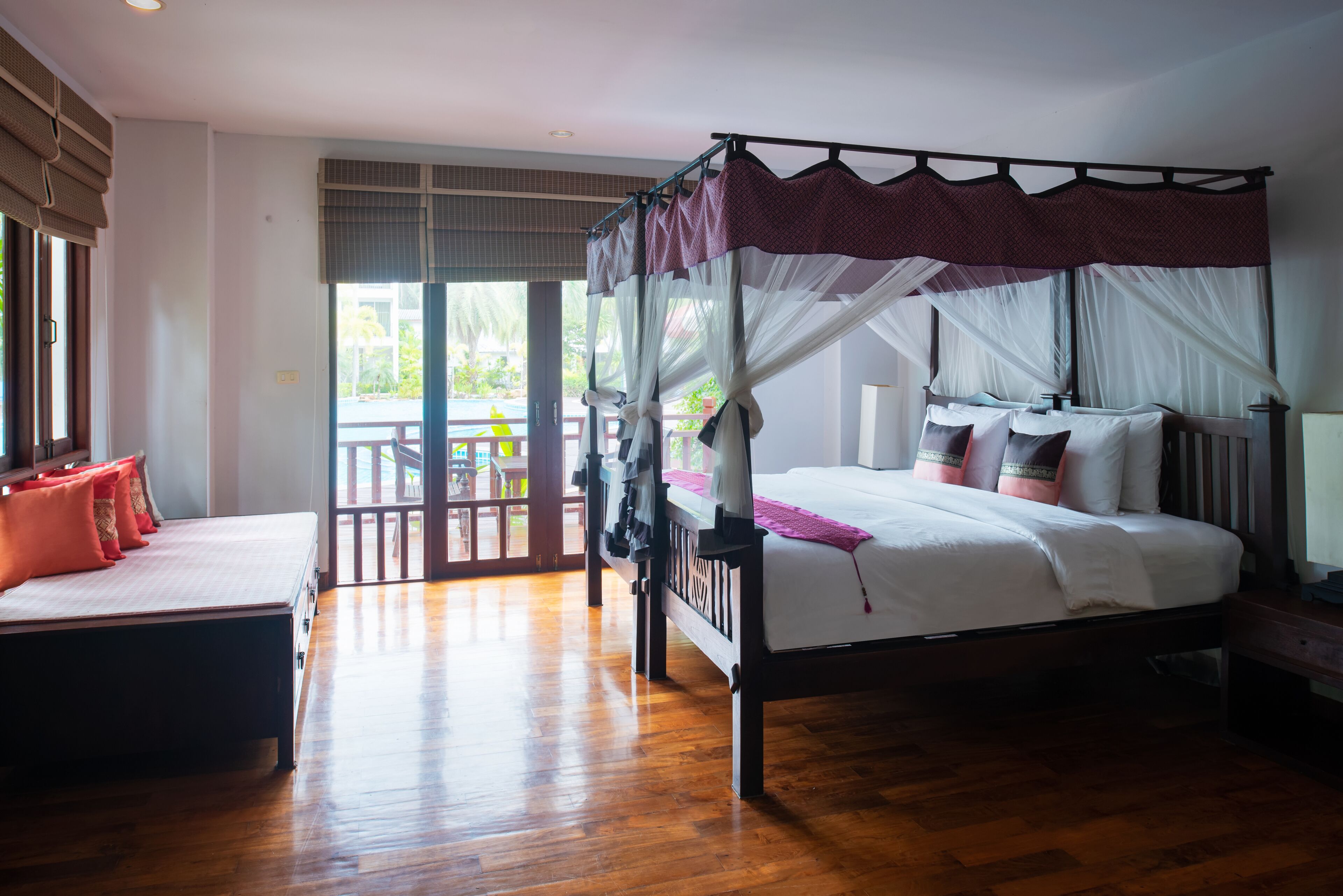A bedroom with a four-poster bed, a daybed, and a view of the outdoors.
