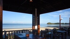 An outdoor seating area with wooden tables and chairs, overlooking a beach and ocean. - Royal Lanta Resort & Spa (Ko Lanta)