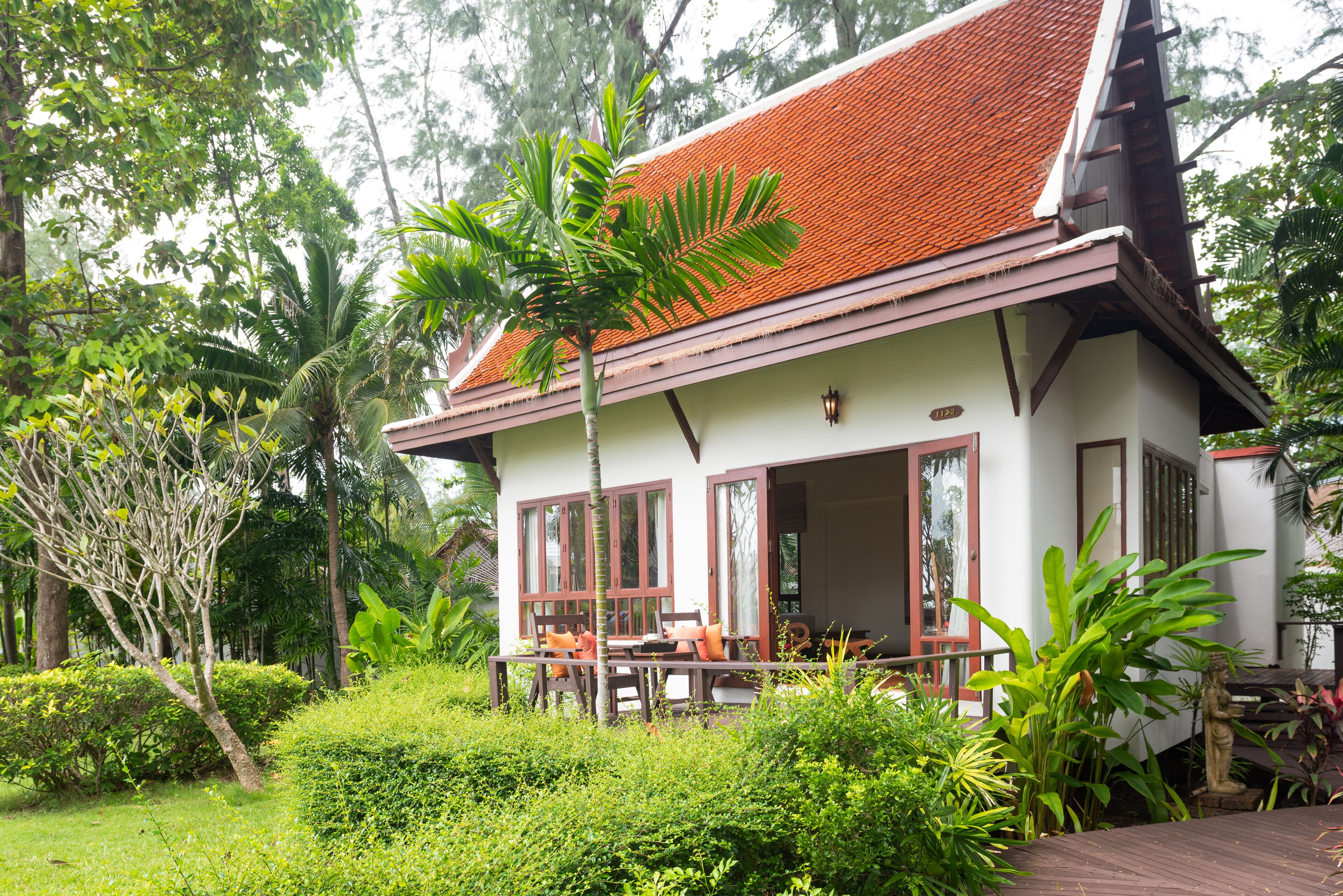 A two-story building with a red tiled roof, large windows, and a porch with wooden furniture.