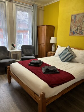 A hotel room with a bed, two armchairs, a wooden wardrobe, a small table with a lamp, and a painting on the wall. - Boscombe Spa Hotel (Bournemouth)