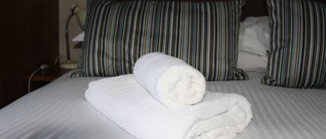 Una cama bien hecha con ropa blanca y almohadas a rayas.