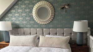 Une chambre à coucher avec un grand lit, deux tables de chevet avec des lampes, un miroir décoratif et un mur orné d’un motif.