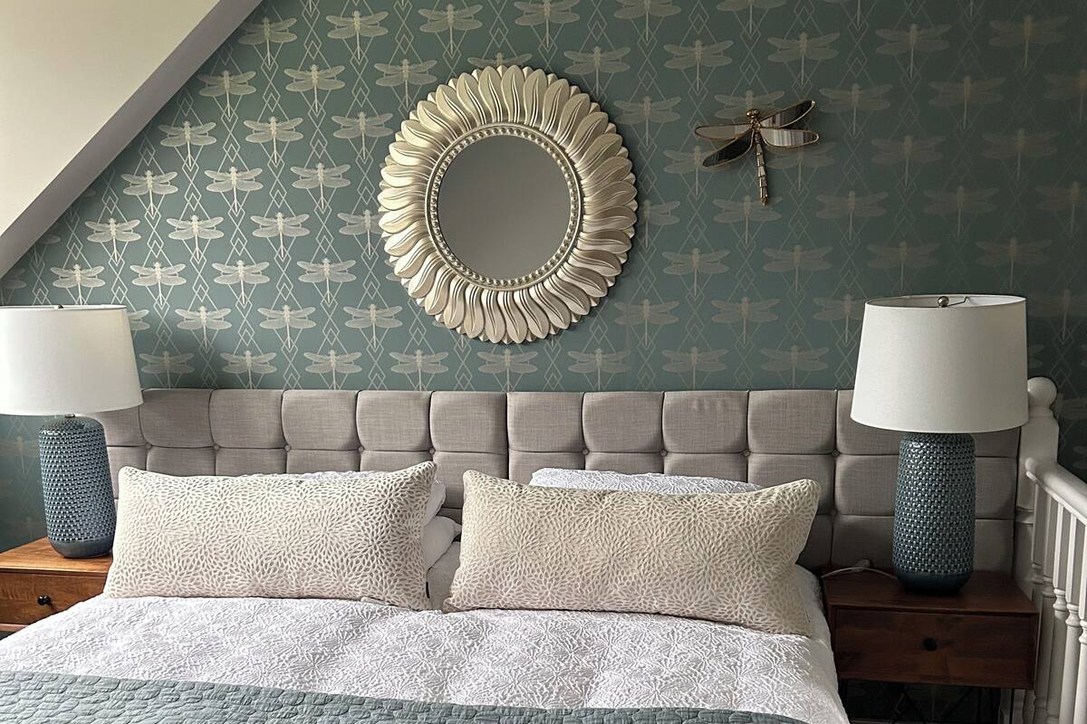A bedroom with a large bed, two bedside tables with lamps, a decorative mirror, and a patterned wall.
