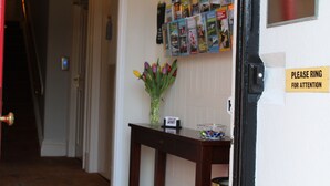 Une zone d'accueil avec une pancarte indiquant « Veuillez sonner pour signaler votre présence », un panneau d'affichage contenant divers éléments et un vase avec des fleurs placé sur une table.