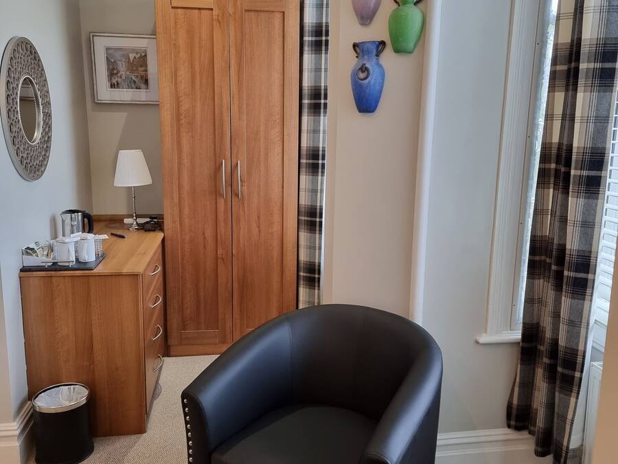 A room with a black leather armchair, wooden wardrobe, and a small table with a lamp.