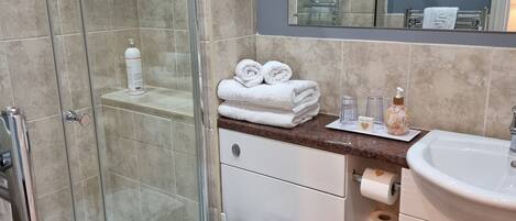 Ein Badezimmer mit Duschkabine aus Glas, Toilette mit Papierhandtuchhalter, Waschbecken mit Spiegel darüber und Handtuchhalter mit gefalteten Handtüchern.