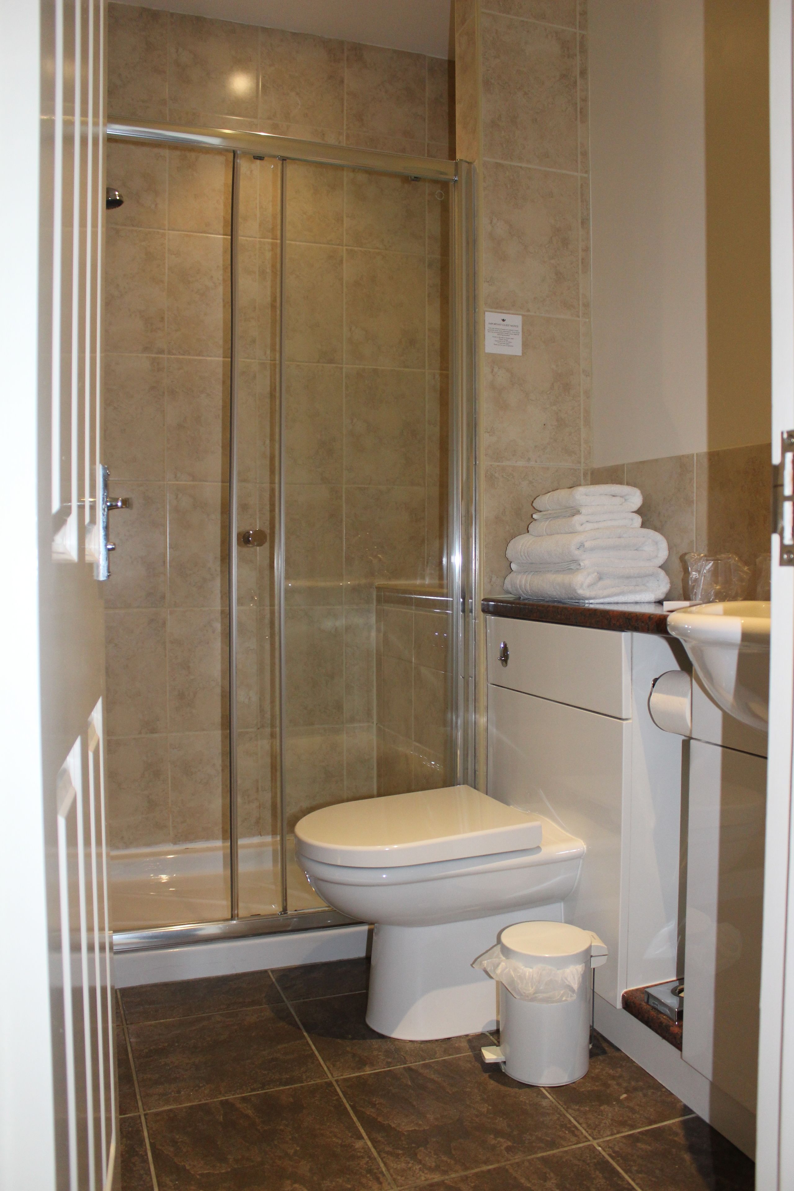 A bathroom with a glass-enclosed shower, a toilet, and a sink with stacked towels.