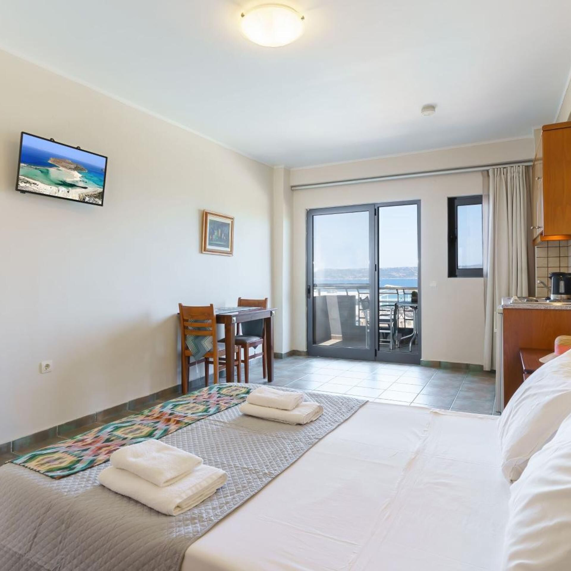 Habitación de hotel con cama, escritorio, silla, vista a través de una puerta corrediza y un cuadro en la pared.