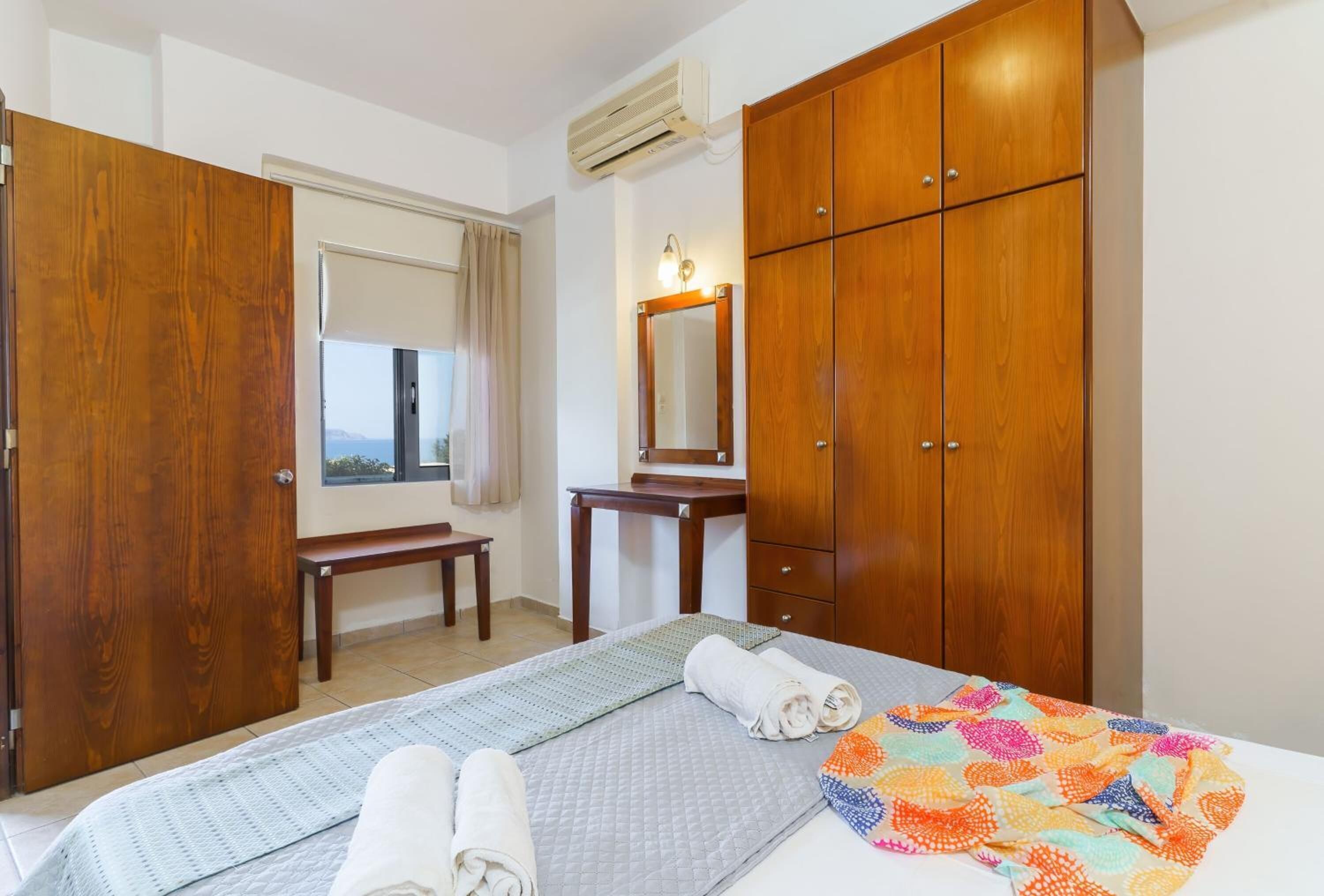 A bedroom with a bed, a bench, a desk, a mirror, and wooden wardrobes.