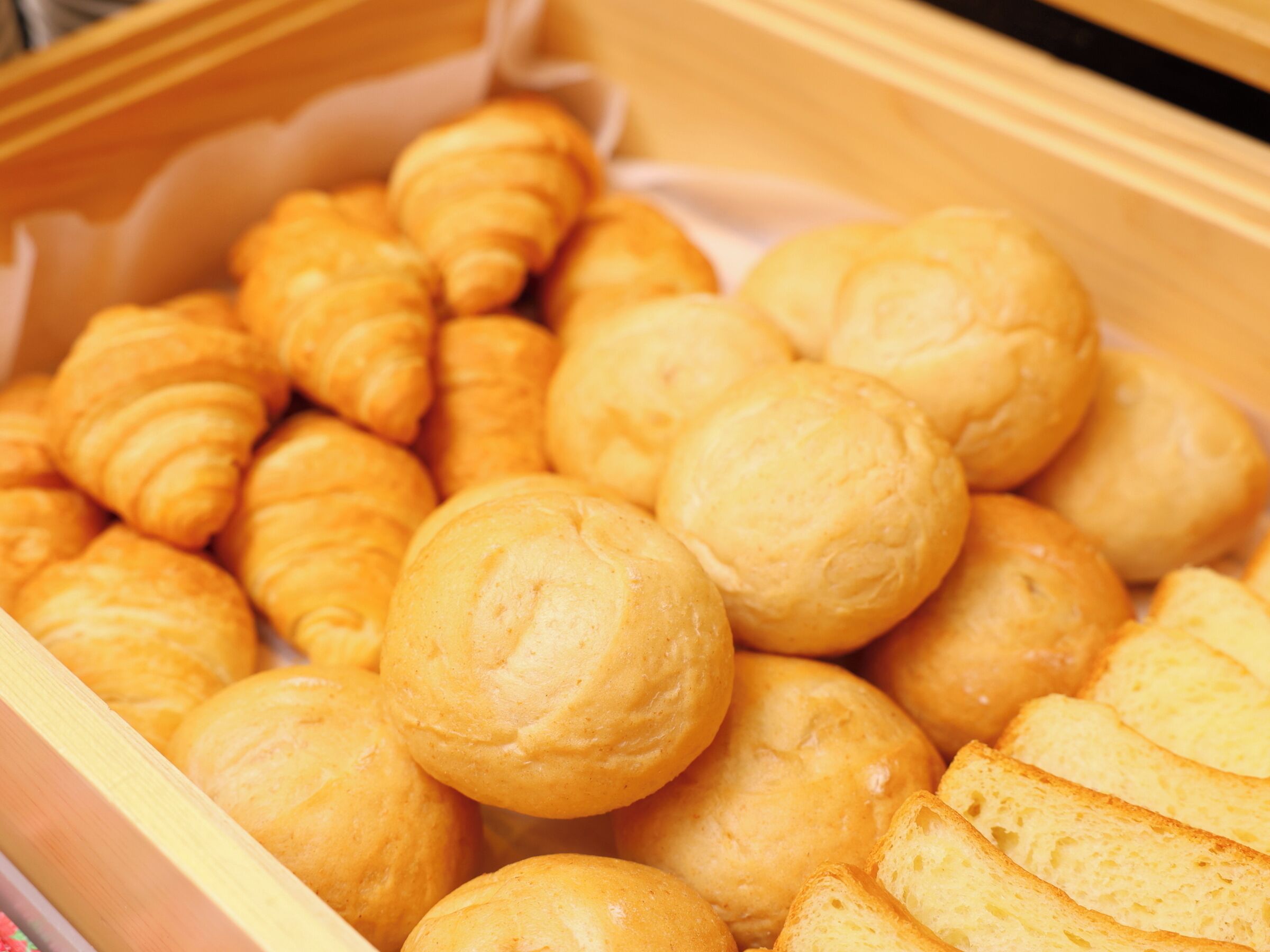 A wooden box filled with golden-brown pastries, including croissants and round bread rolls.