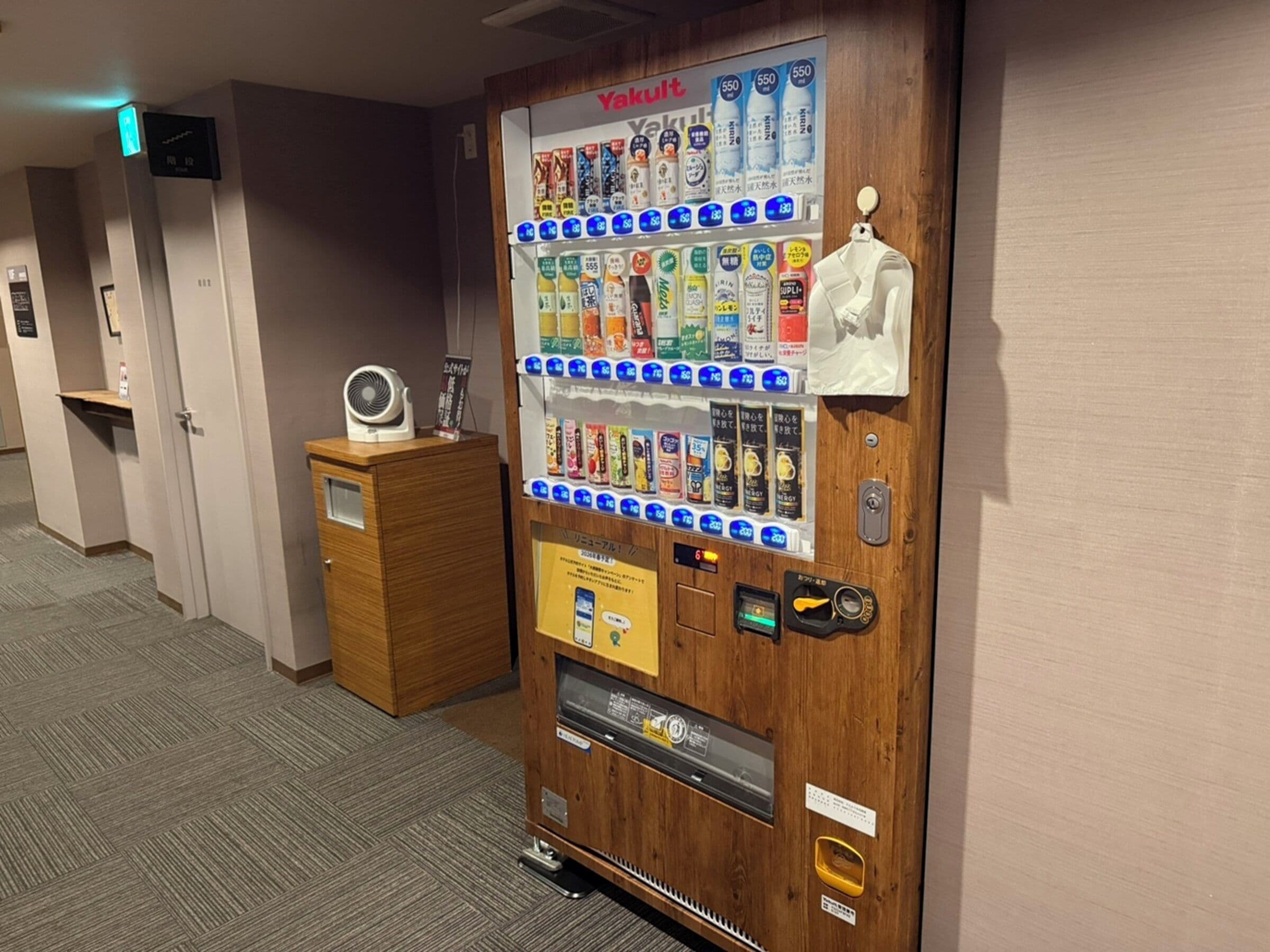 Un distributeur automatique proposant diverses boissons, avec un petit ventilateur fixé à un meuble en bois.