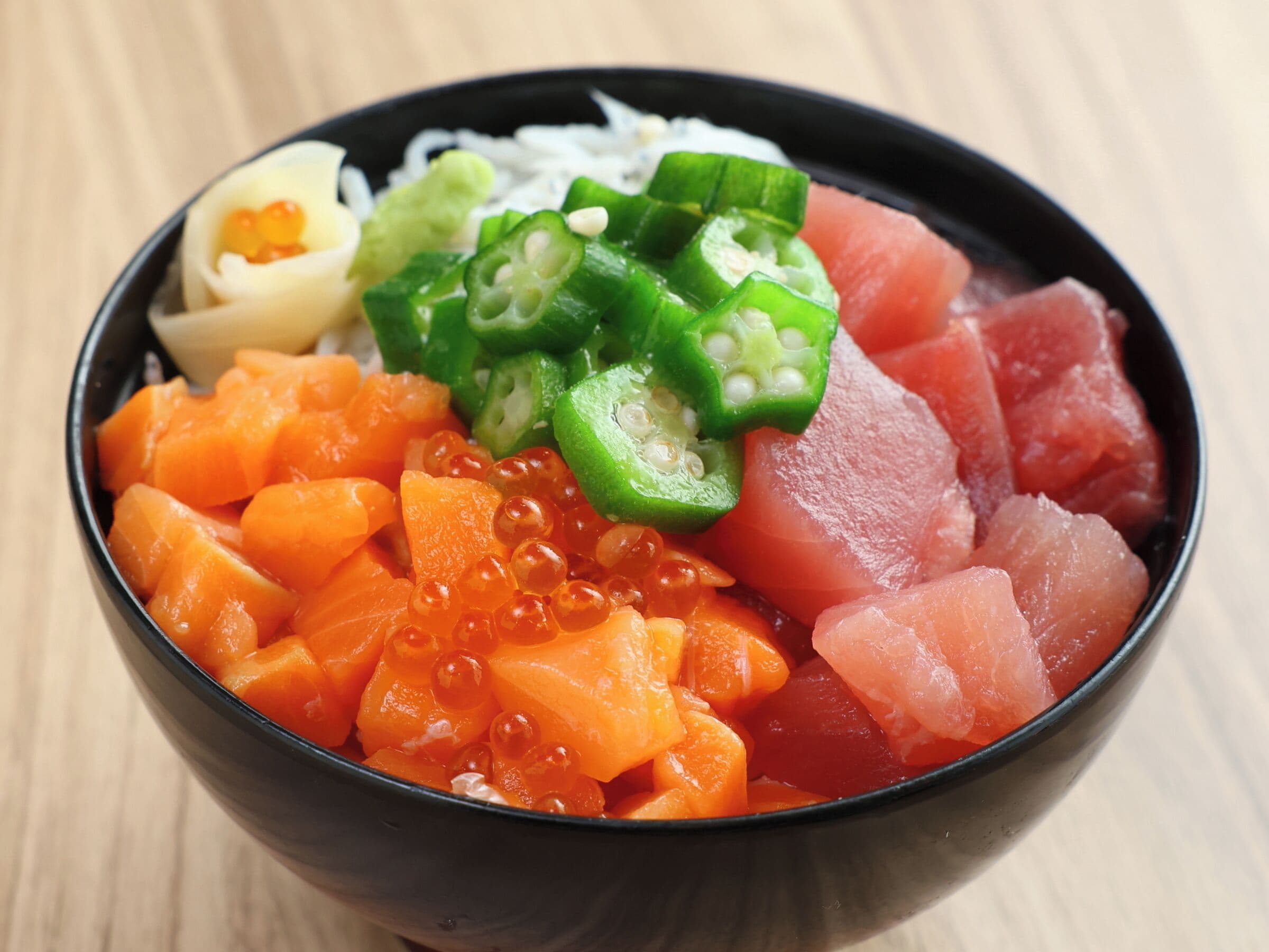 Een schaal sashimi met oranje vis, groene pepers en roe.