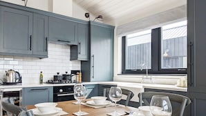 A modern kitchen with grey cabinets, a wooden dining table set for four, and a window with a view of the outside. - Retallack Resort (St. Columb Major)
