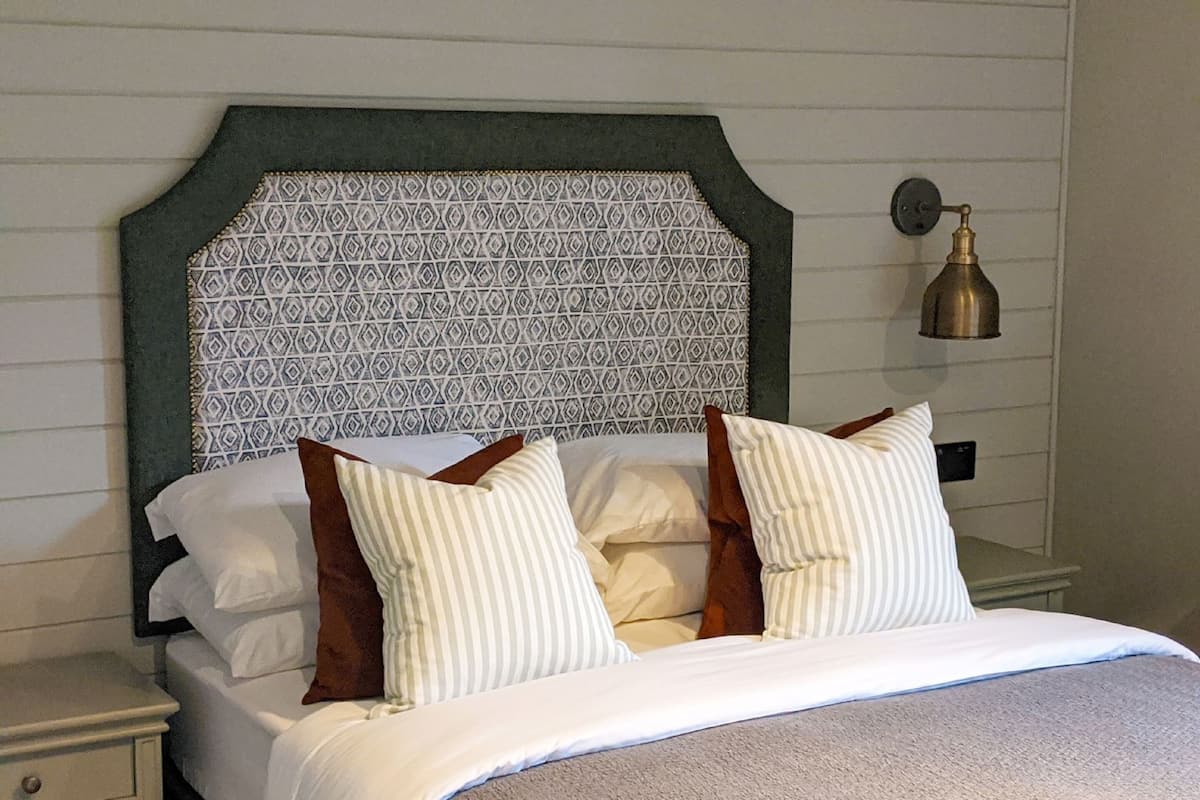 A bed with a patterned headboard, white bedding, and striped pillows.