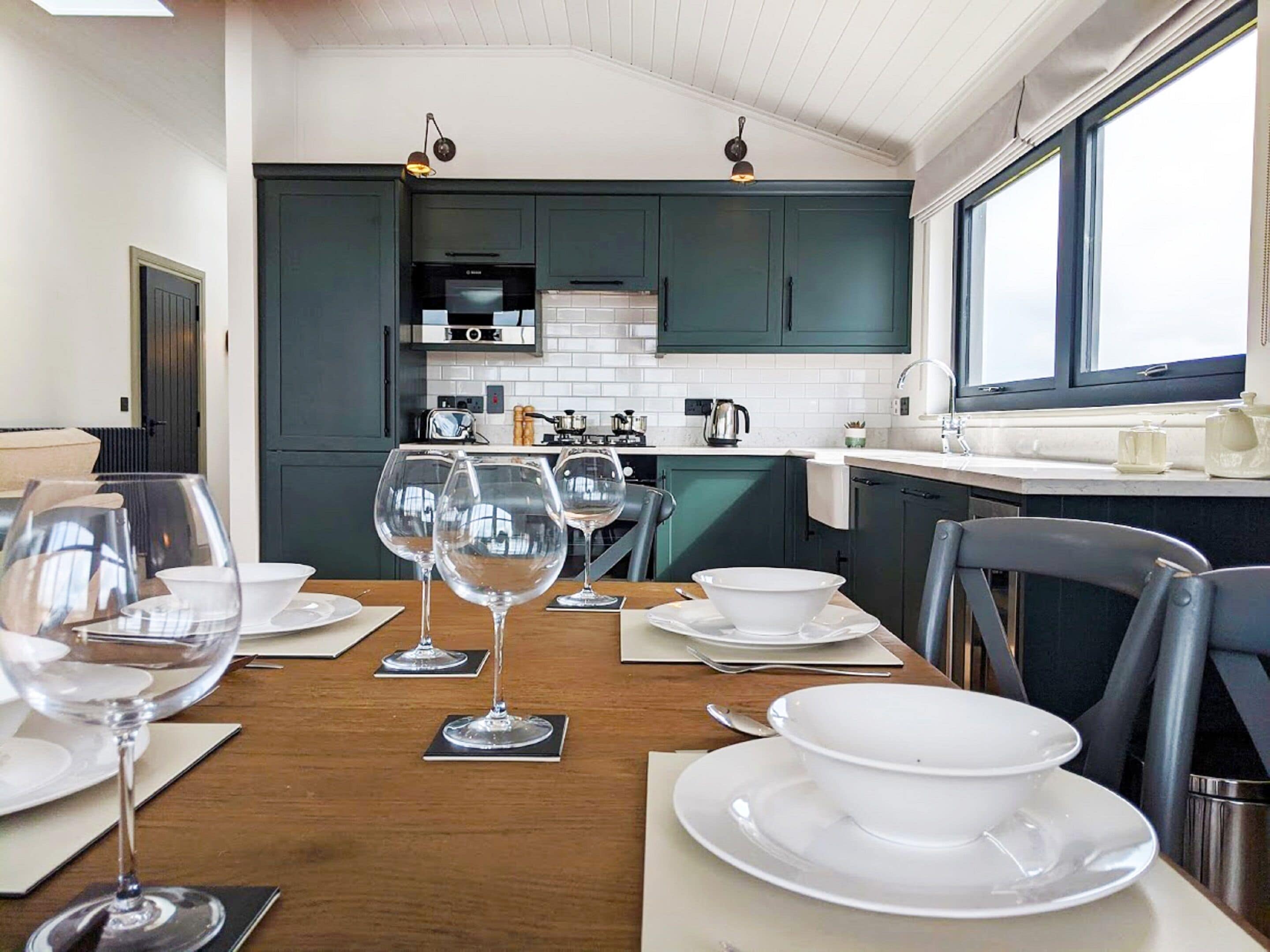 A modern kitchen with dark green cabinets, white countertops, and a dining area with a wooden table set for four.