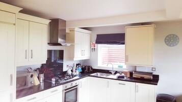 A kitchen with white cabinets, a stove, a sink, and a window with blinds.