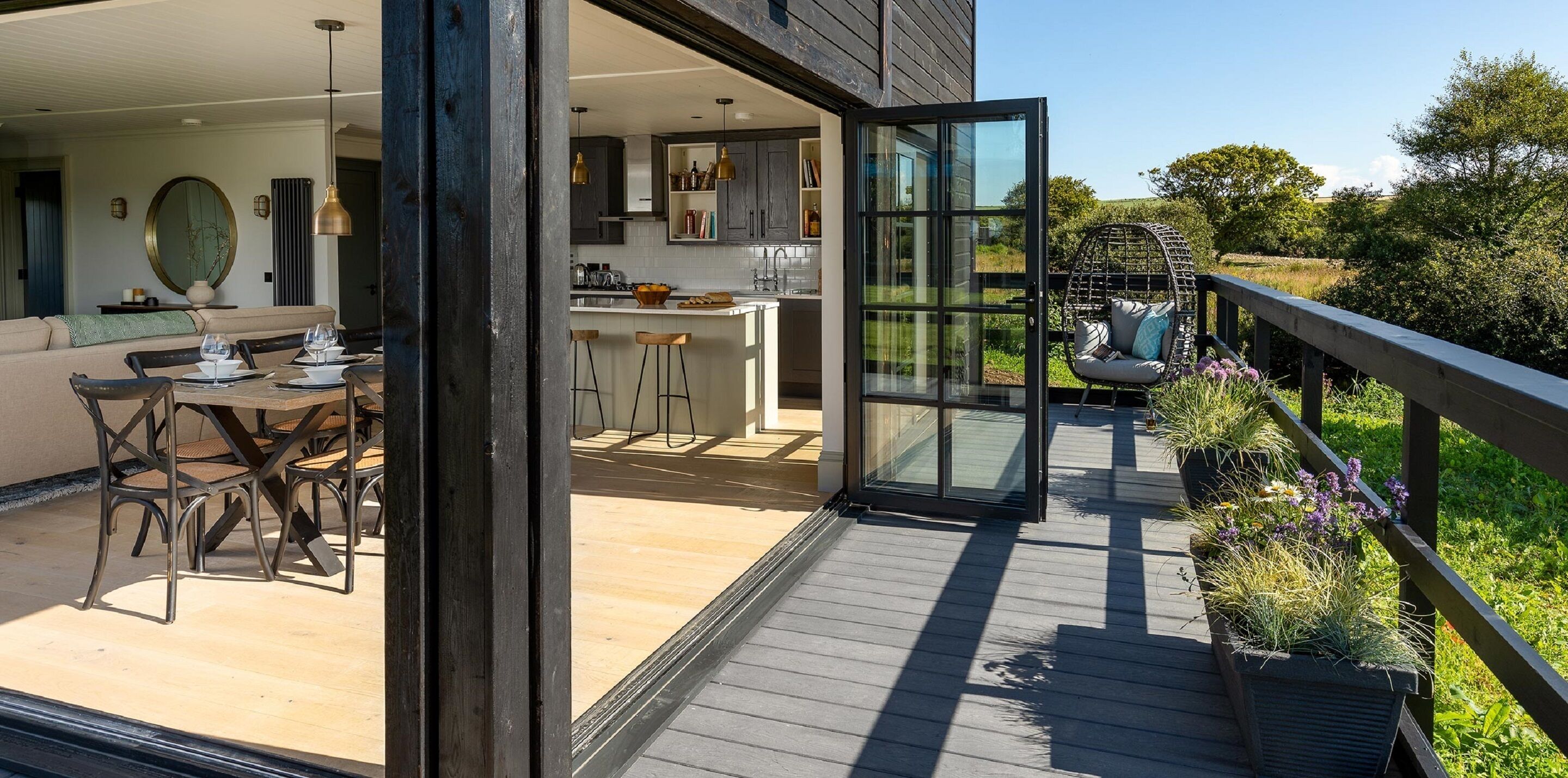 An open-plan living area with a dining table and chairs, a kitchen with modern appliances, and a balcony with plants and a swing chair.