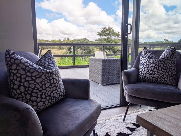 A balcony with a sofa and armchair, both with patterned cushions, and a wicker table.