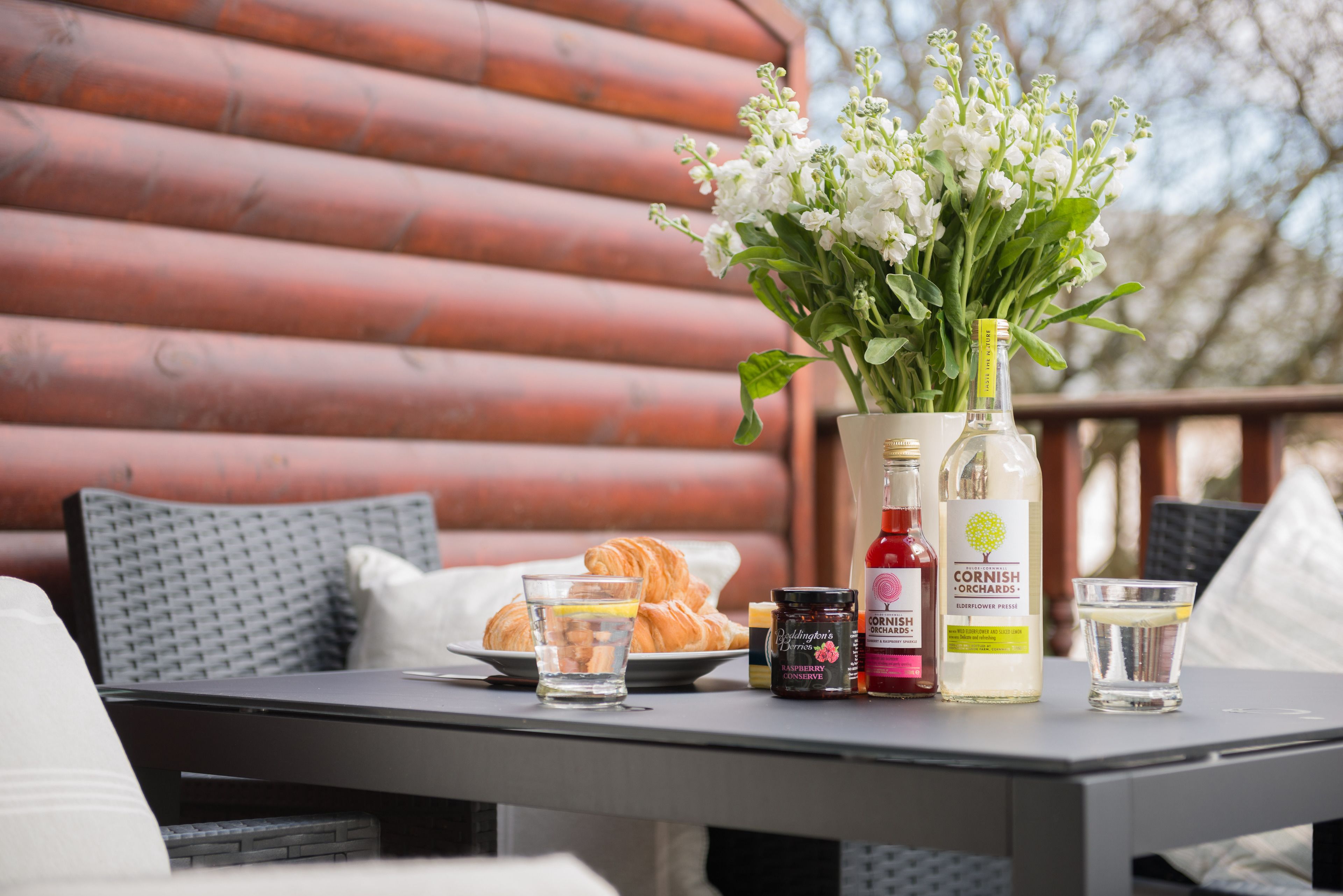 A table with croissants, a bottle of Cornish Orchards, a jar of jam, and a glass of water.