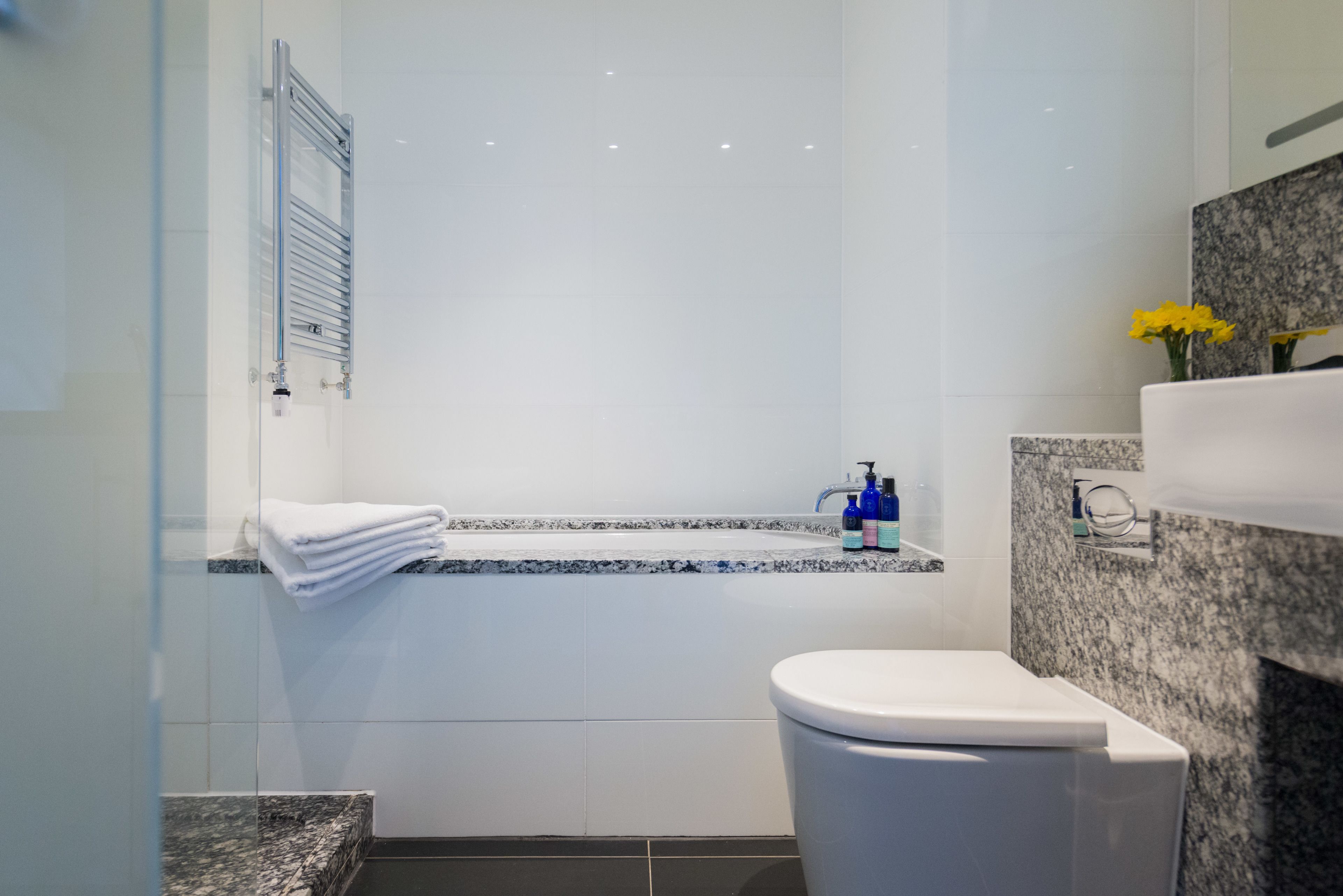 A modern bathroom with a glass shower enclosure, a white toilet, a marble countertop, and a granite backsplash.