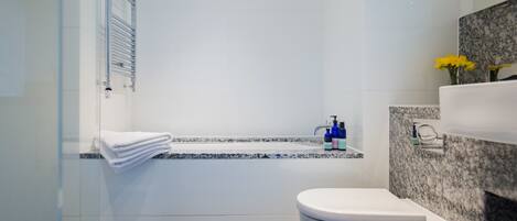 A modern bathroom with a glass shower enclosure, a white toilet, a marble countertop, and a granite backsplash.