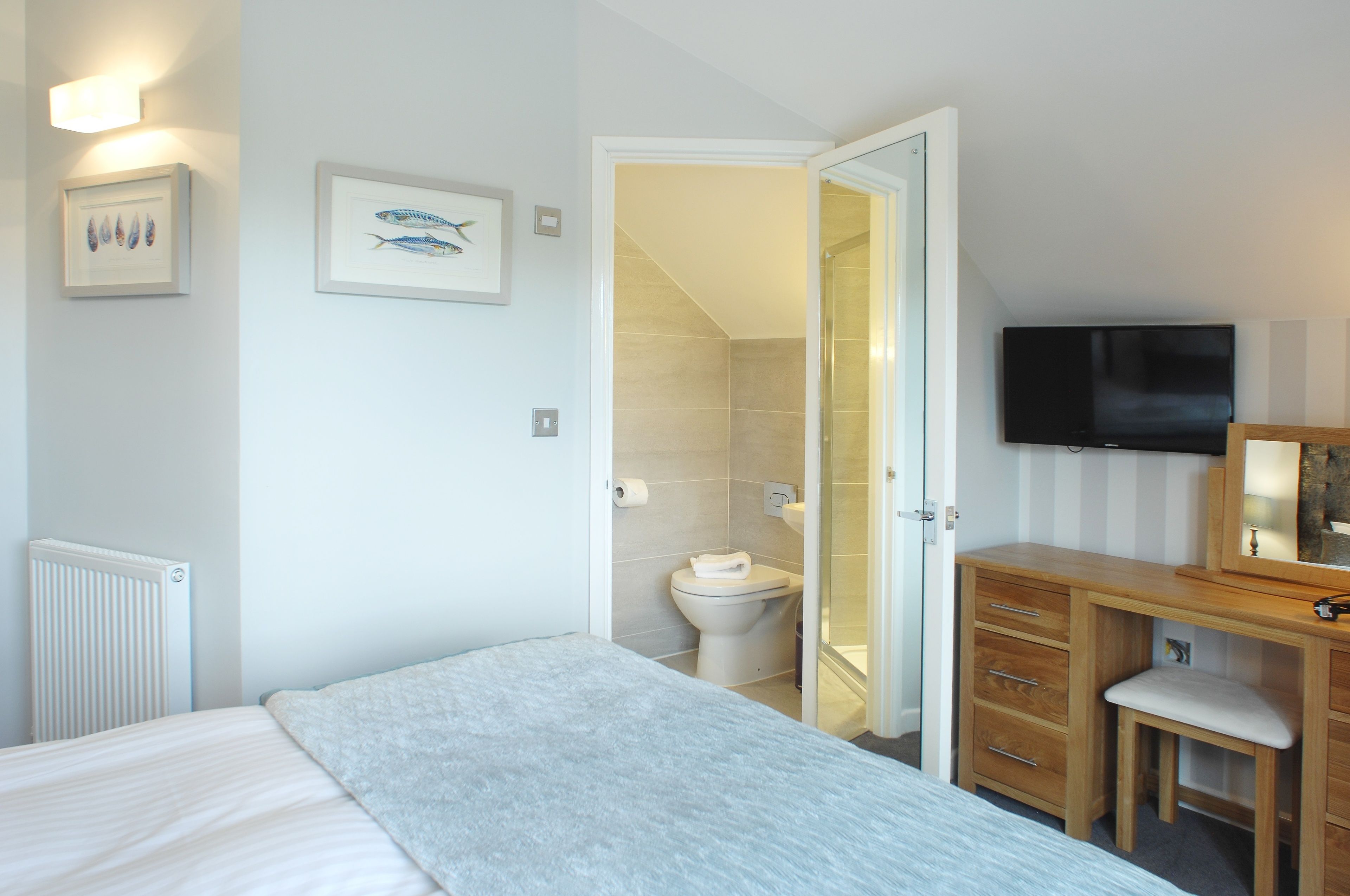 Un dormitorio con cama, cómoda de madera, televisor y baño visible a través de una puerta abierta.