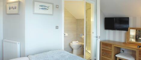 A bedroom with a bed, a wooden dresser, a television, and a bathroom visible through an open door.