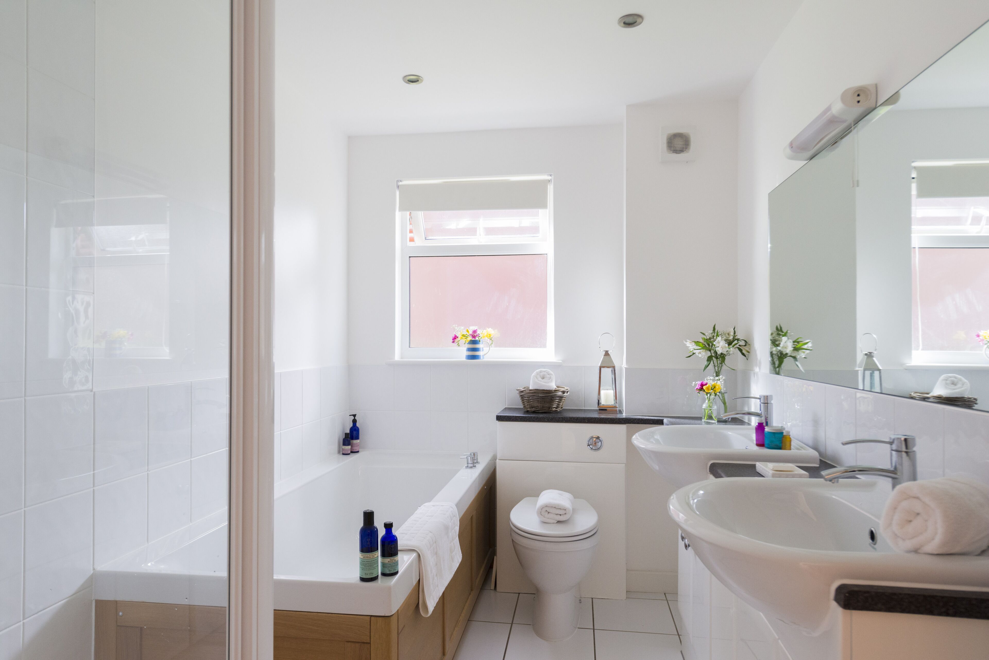 A modern bathroom with a bathtub, toilet, and two sinks.