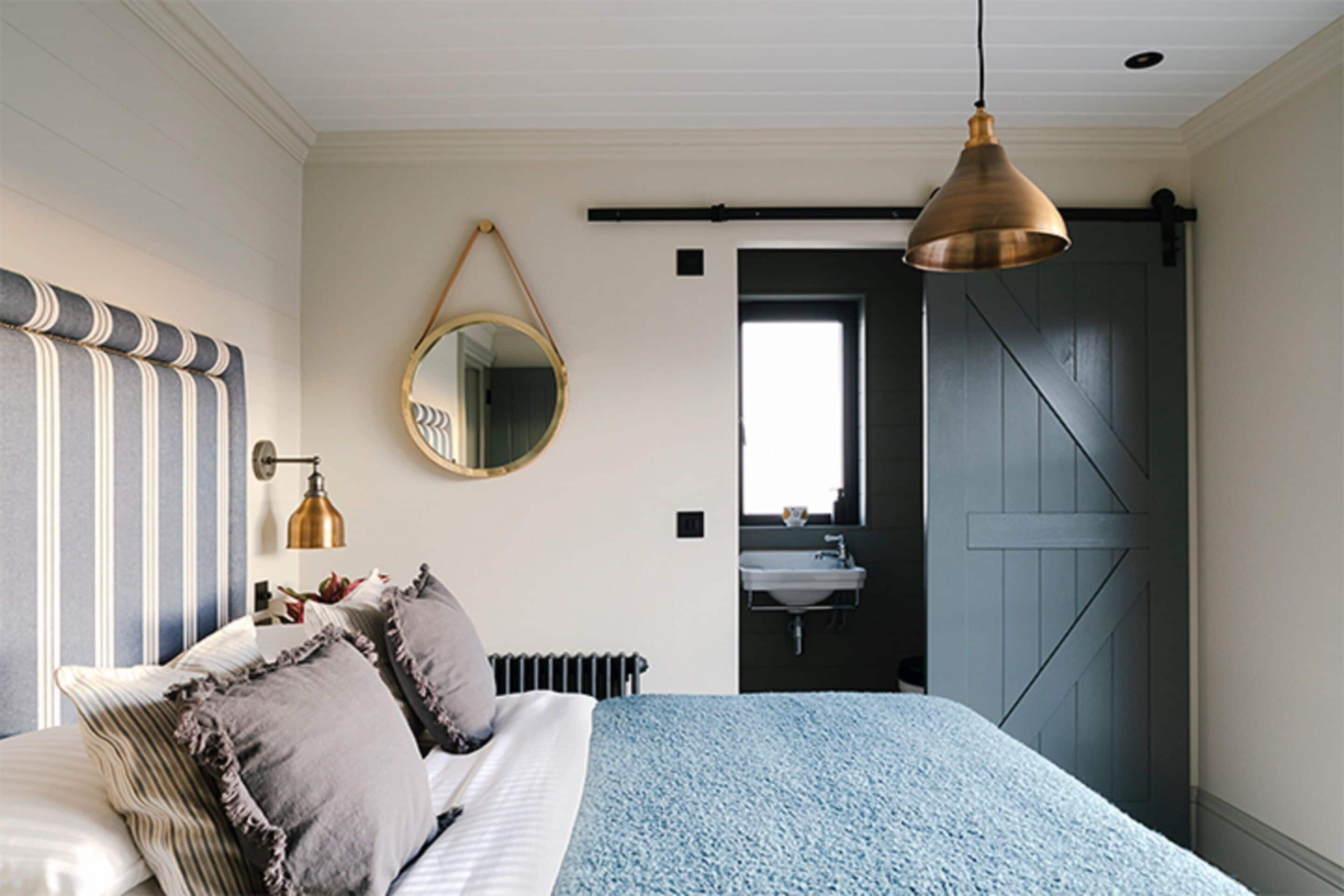Een slaapkamer met een bed, een spiegel, een hanglamp, een radiator en een deur naar een badkamer.