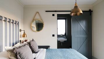 A bedroom with a bed, a hanging mirror, a pendant light, a radiator, and a door leading to a bathroom.