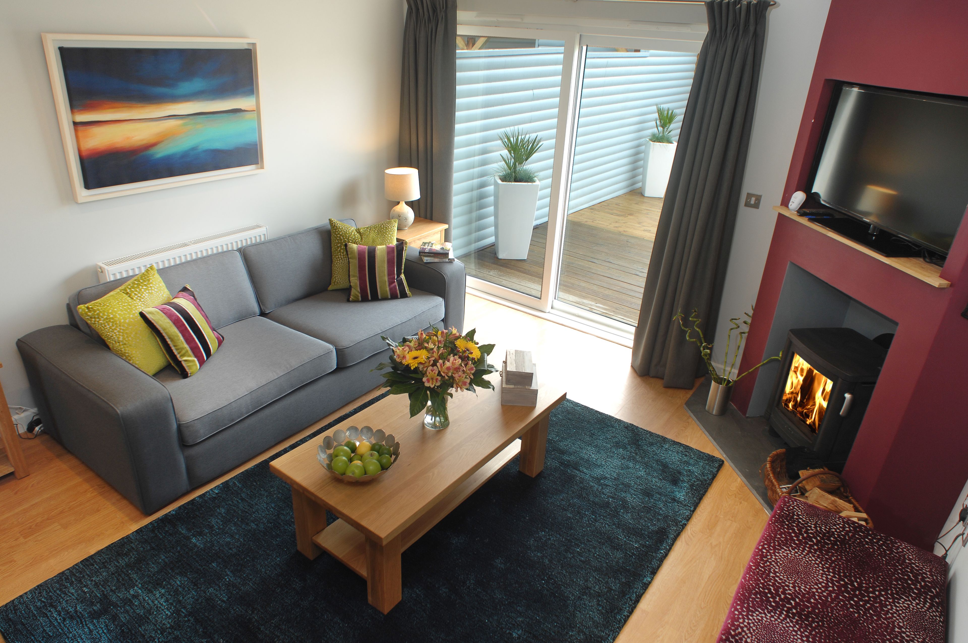 A modern living room with a grey sofa, a wooden coffee table with fruit, a TV, and a fireplace.