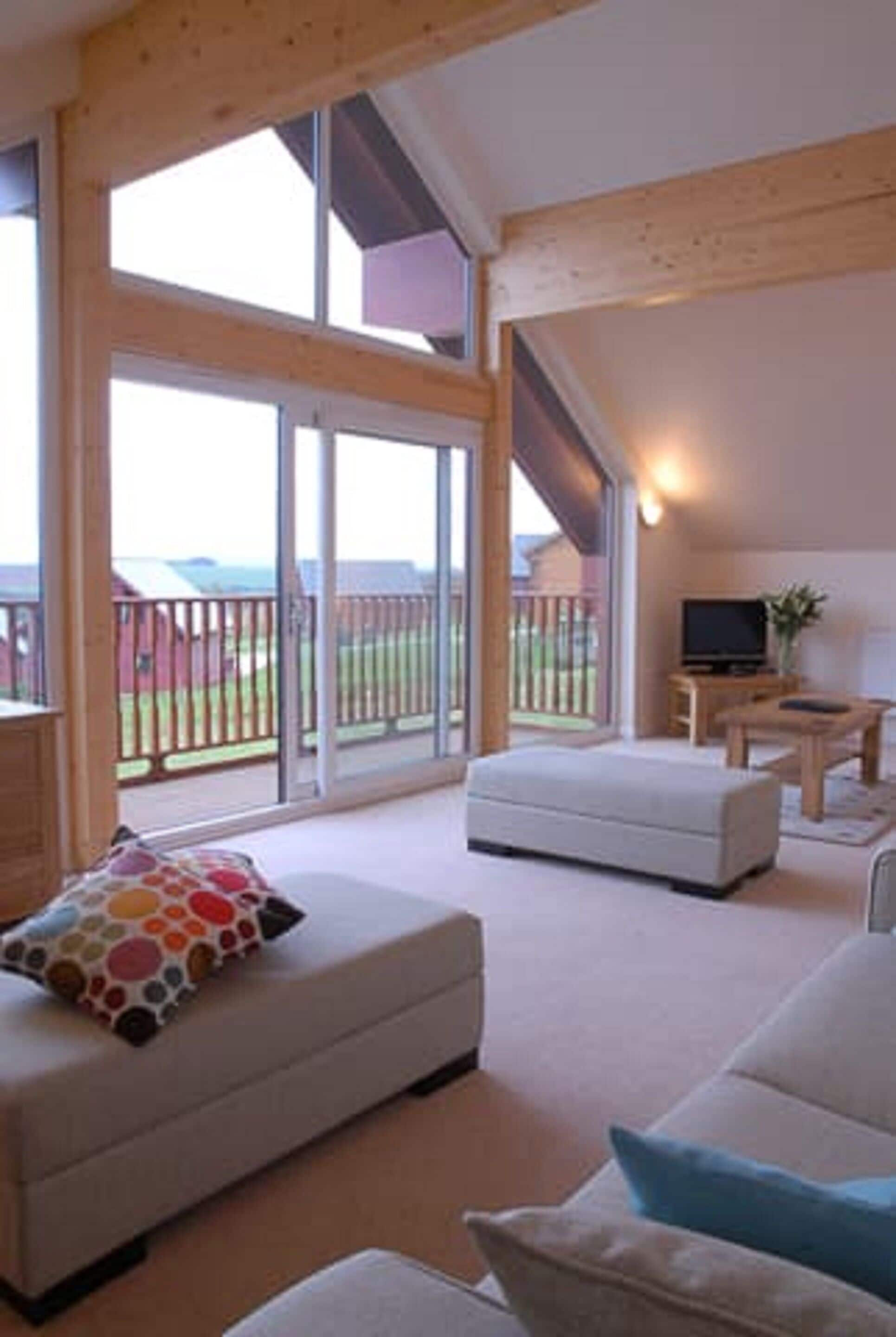 A spacious living area with a large sliding glass door leading to a balcony, a flat-screen TV, and a wooden coffee table.
