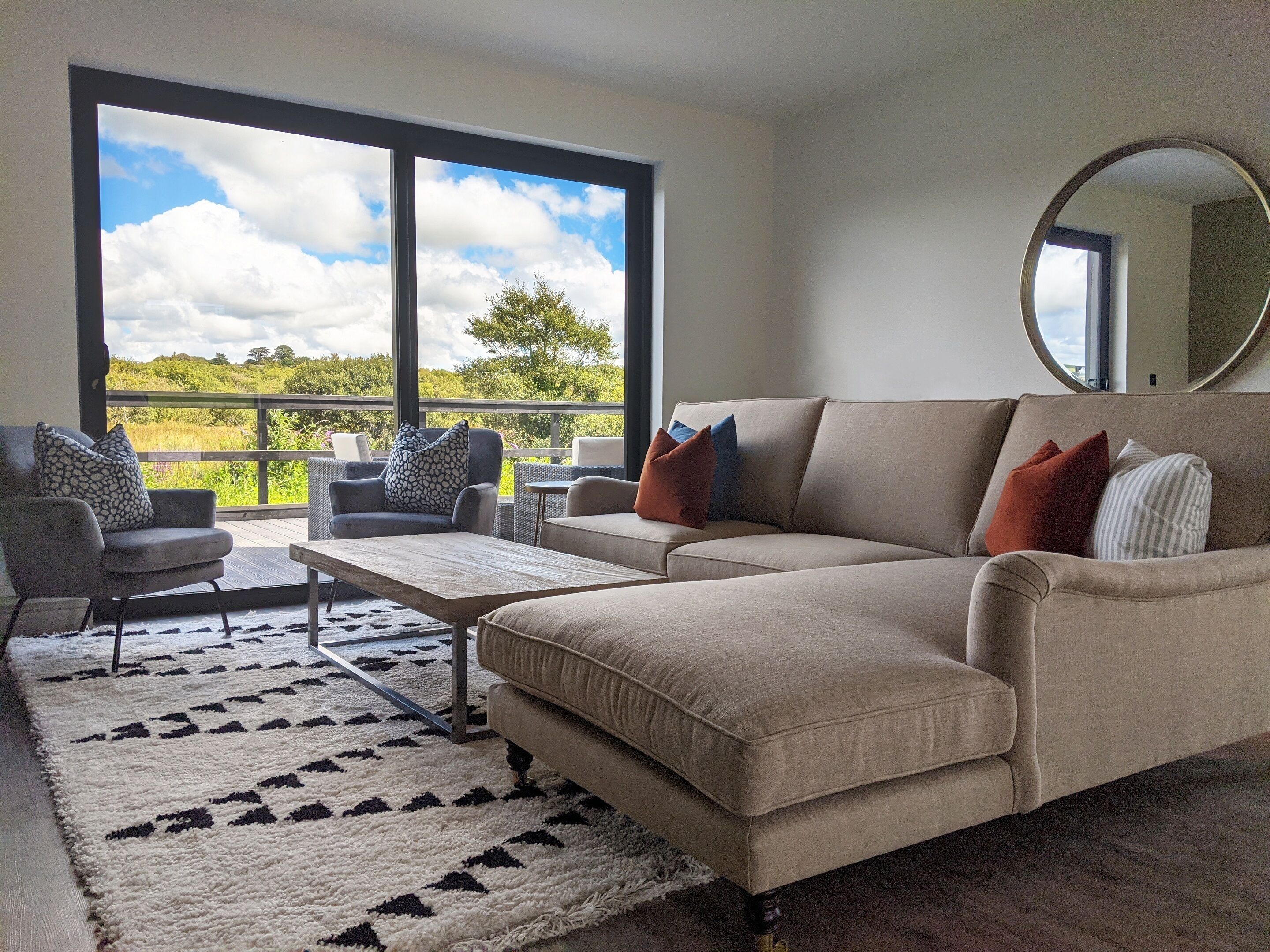 A living room with a beige sofa, two armchairs, a coffee table, and a large window offering a view of a green landscape.