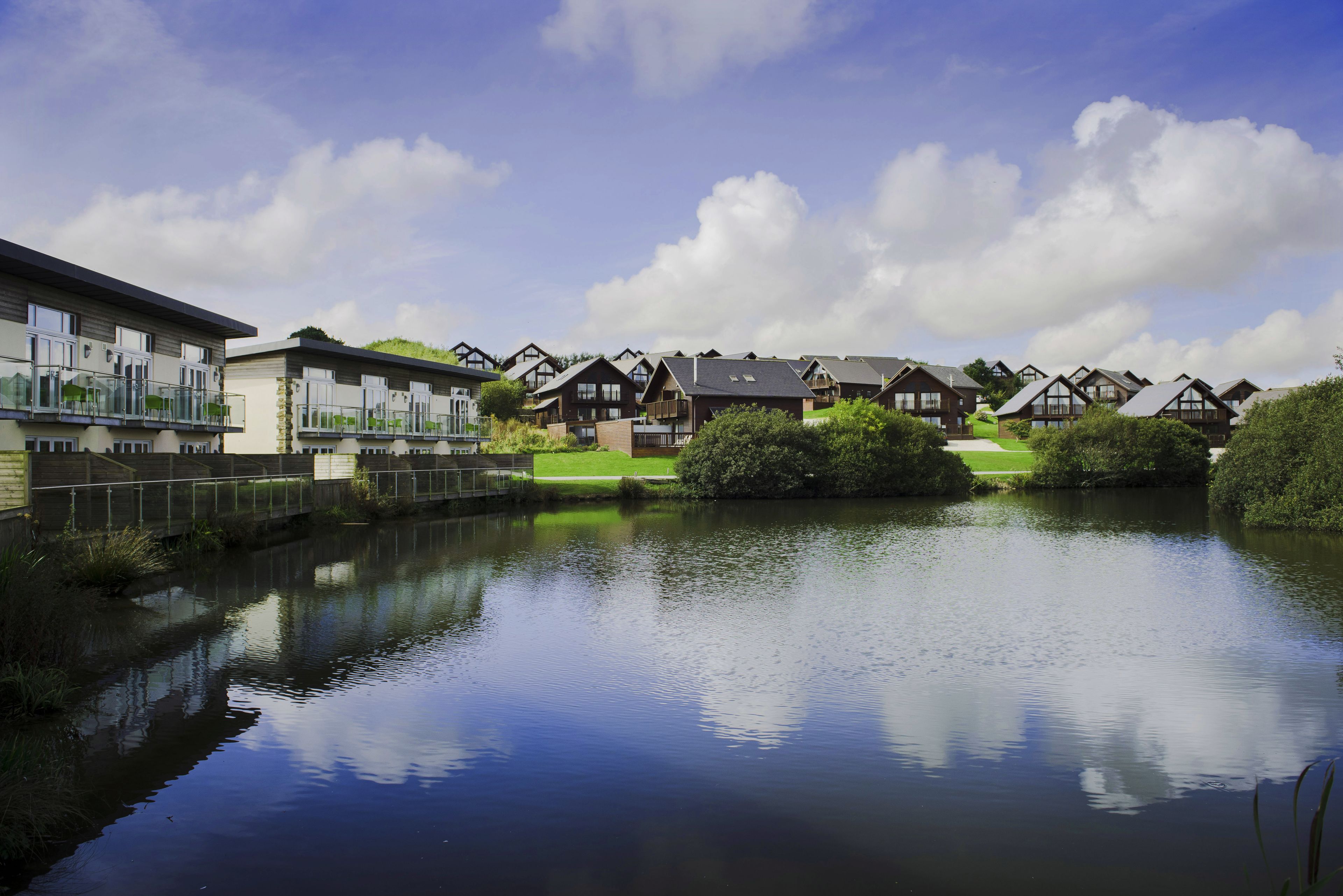 A lakeside residential area with modern and traditional houses, a bridge, and a calm water body reflecting the sky.