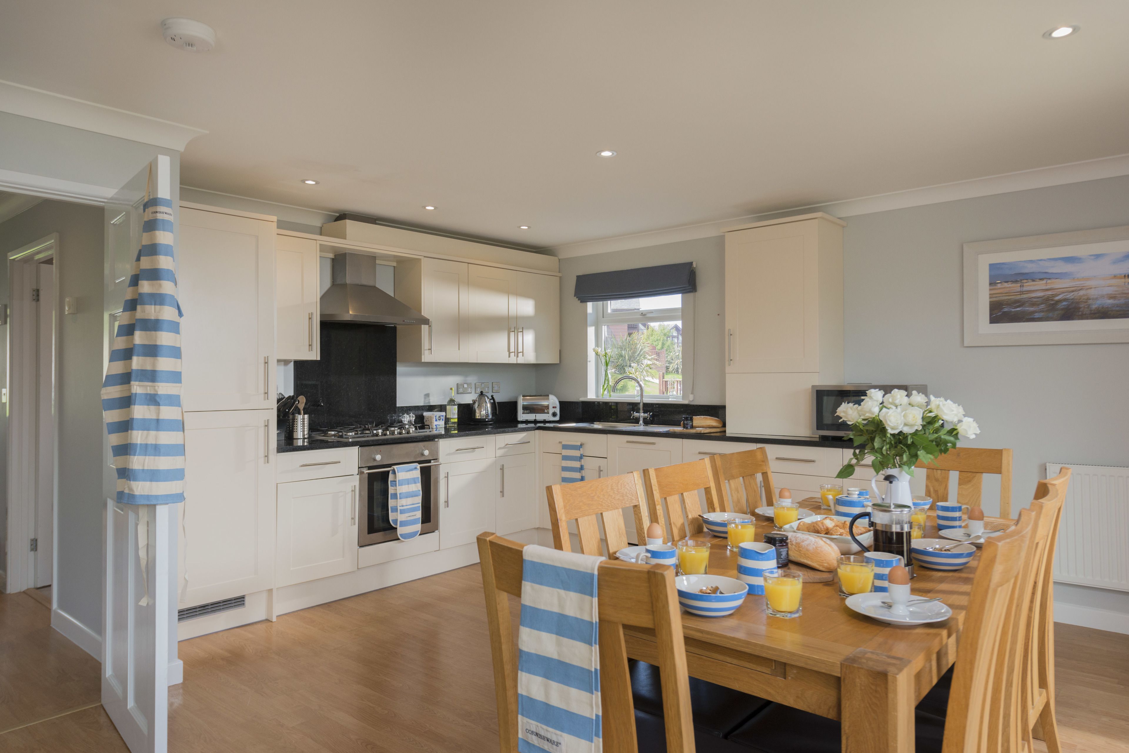 A modern kitchen with white cabinets, a black countertop, and wooden chairs.