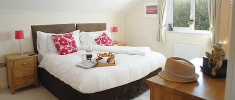 A bedroom with a large bed, bedside tables, a window with curtains, and a view of greenery outside.