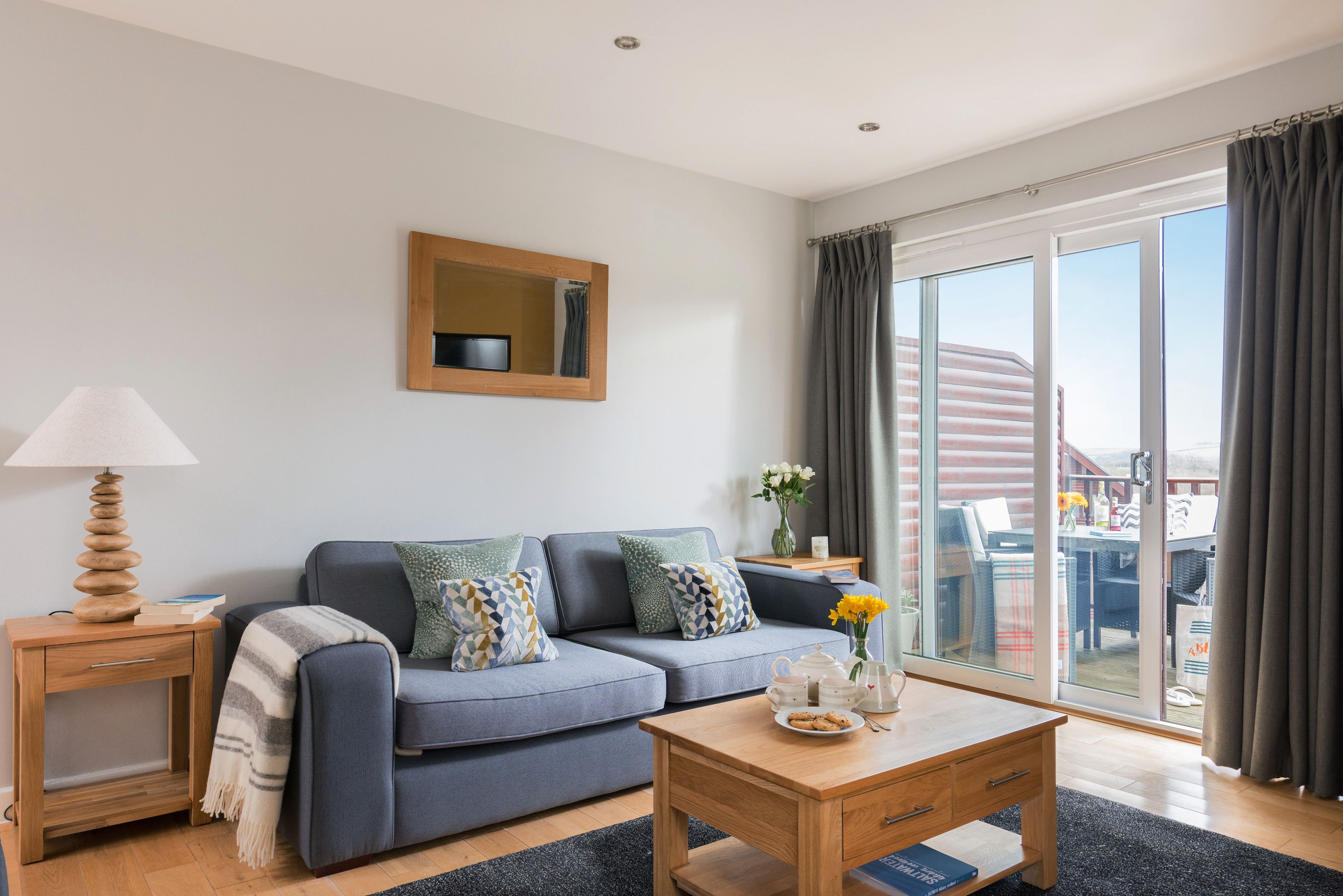 Een moderne woonkamer met een bank, een houten bijzettafeltje, een salontafel en een schuifdeur naar een terras.