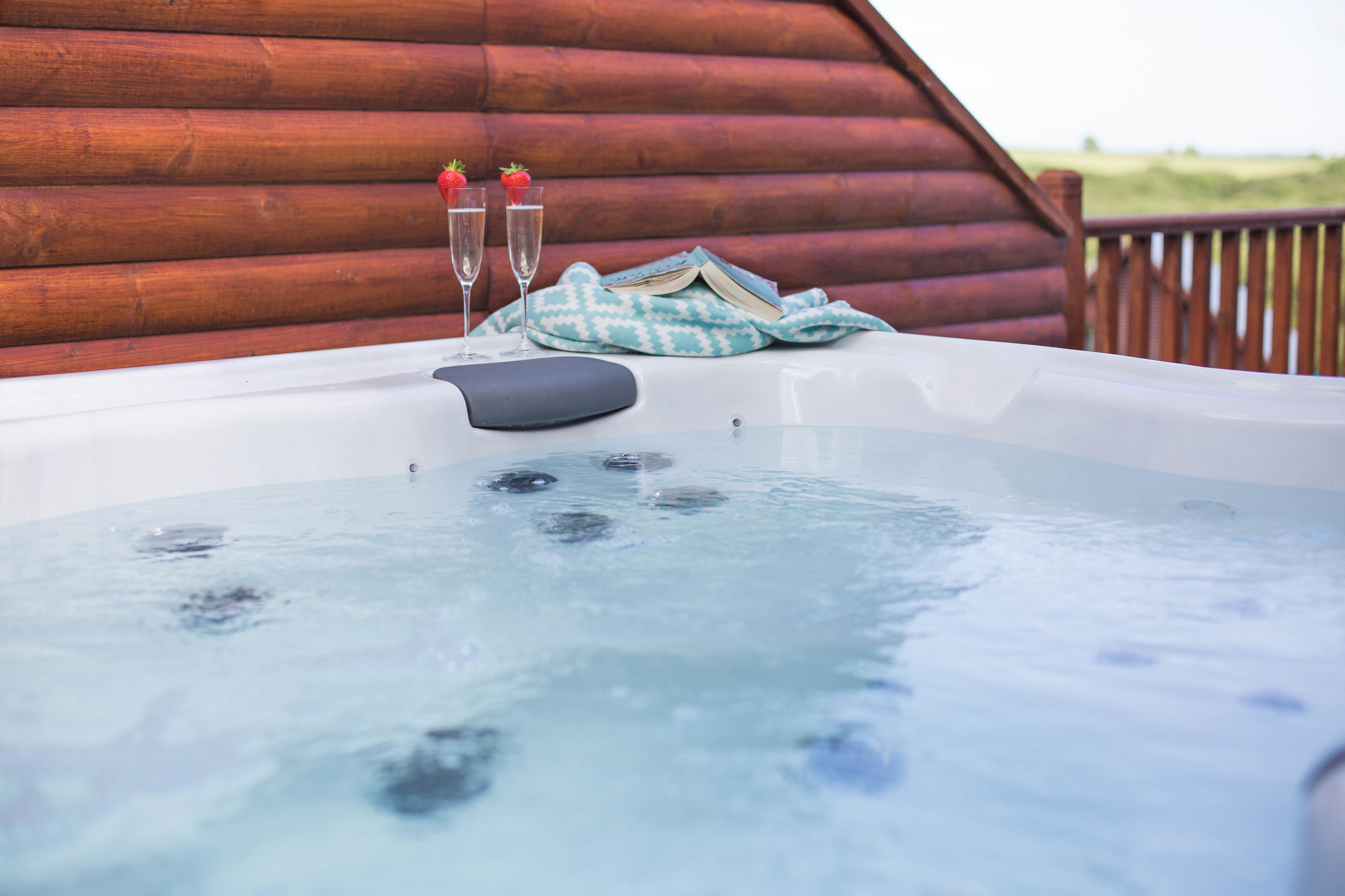 A hot tub with two champagne glasses and strawberries, set against a wooden cabin backdrop.