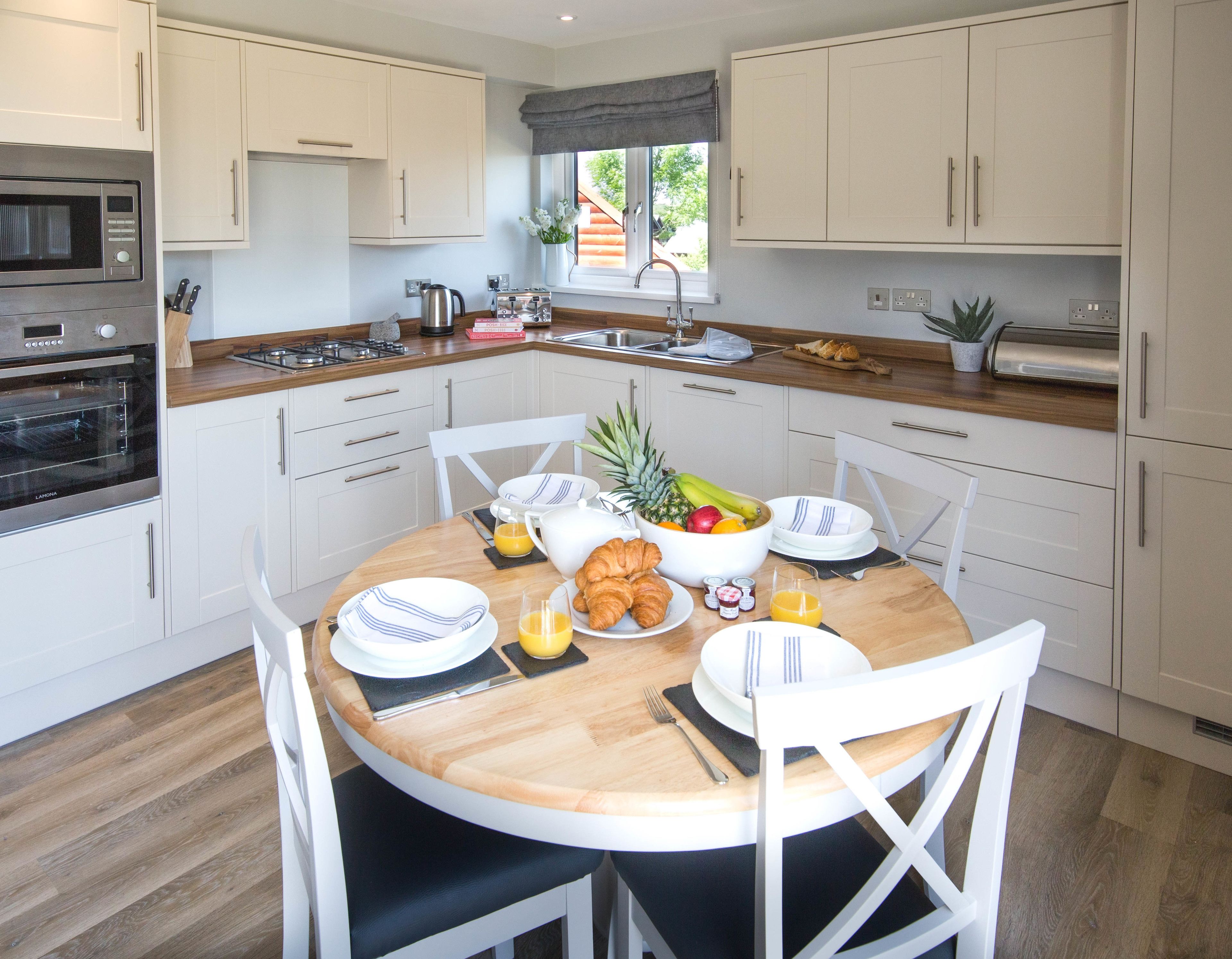 A modern kitchen with white cabinets, a wooden countertop, and a breakfast setup including fruits, croissants, and orange juice.