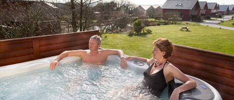 Two people in a hot tub outdoors with a grassy yard and houses in the background.