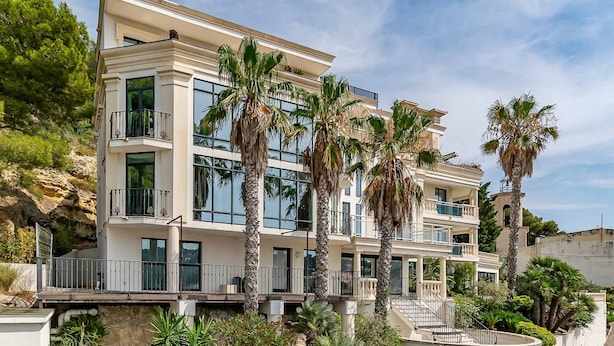 Un edificio de varios pisos con balcones, ventanas amplias y palmeras.