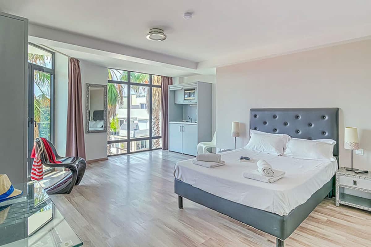 Ein modernes Hotelzimmer mit einem großen Bett, einem Schreibtisch mit Stuhl, einem Kleiderschrank und Blick ins Freie.