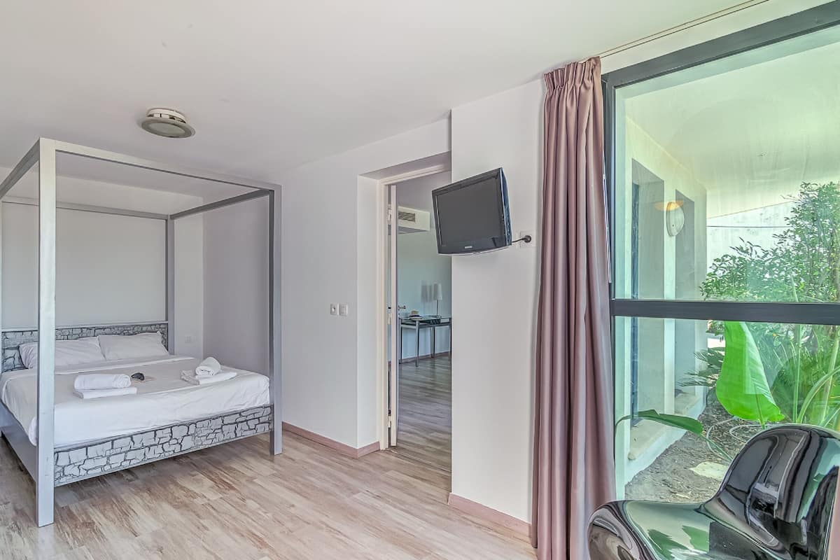 Ein modernes Schlafzimmer mit einem Himmelbett, einem Flachbildfernseher und Blick ins Grüne.