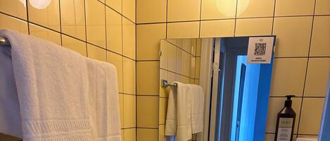A bathroom with yellow tiles, a white sink, a mirror, a towel rack, a small trash can, and a toilet.