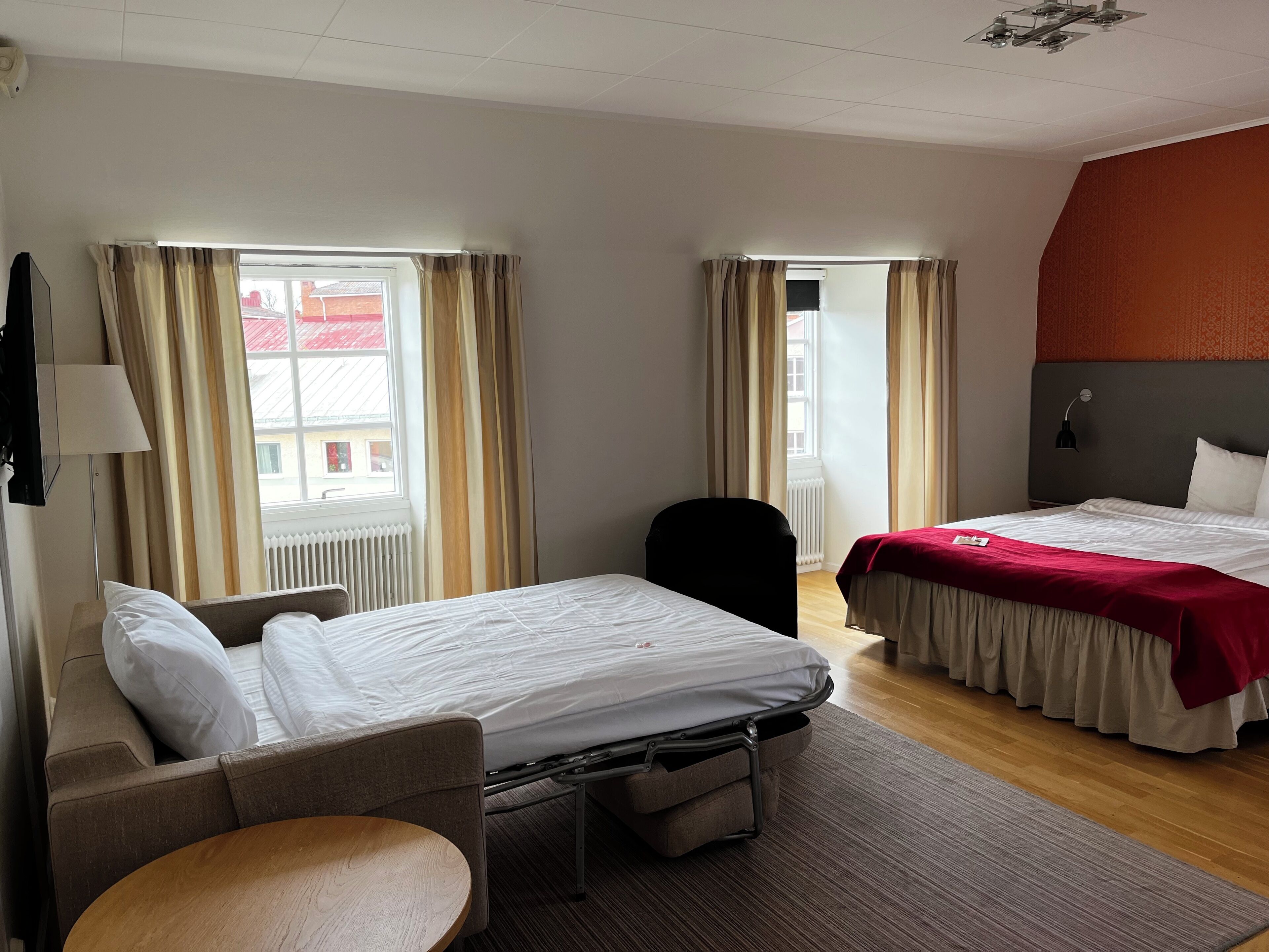 A hotel room with two beds, a chair, a small table, and a window with curtains.