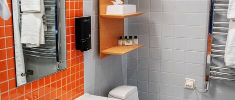 Un baño con lavamanos blanco, espejo y retrete. Las paredes tienen azulejos naranja y gris, y el piso es de cuadros negros y blancos.