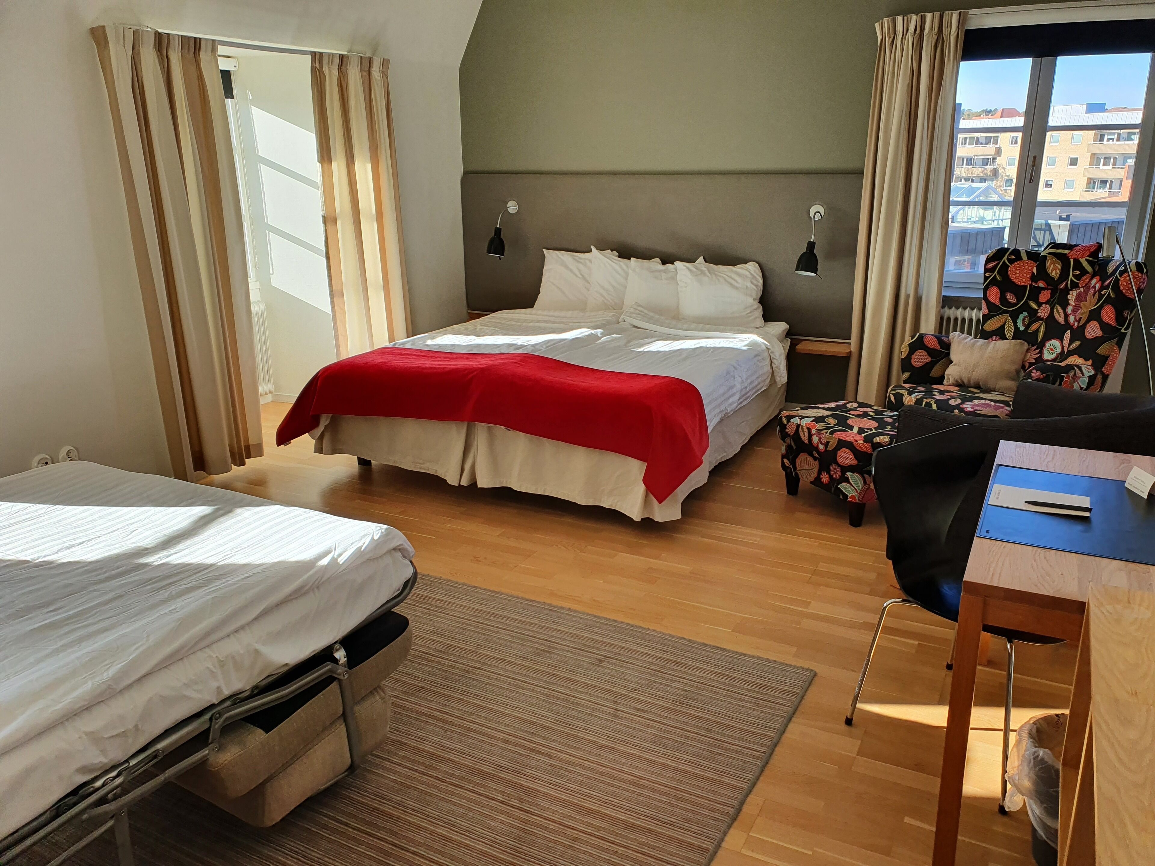 A hotel room with a bed, a desk, a chair, and a window.