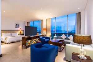 Habitación de hotel moderna con una cama grande, televisor, escritorio y zona de estar.
